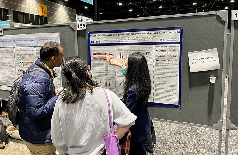 Yiqun presenting research poster to two people at AGU